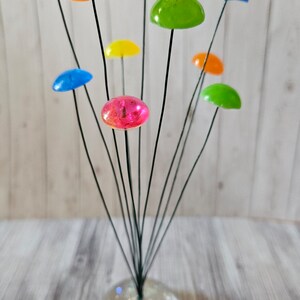 K&ouml;nnte beinhalten: Eine farbige Glaspilzskulptur mit einem klaren Glasfu&szlig;. Die Pilze sind in verschiedenen Farben, darunter Rot, Orange, Gelb, Gr&uuml;n und Blau.
