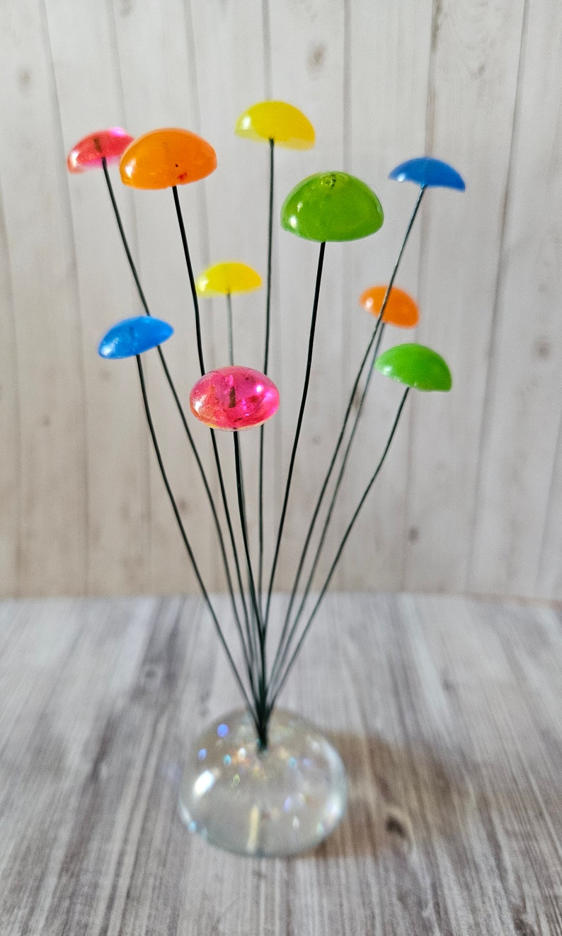 K&ouml;nnte beinhalten: Eine farbige Glaspilzskulptur mit einem klaren Glasfu&szlig;. Die Pilze sind in verschiedenen Farben, darunter Rot, Orange, Gelb, Gr&uuml;n und Blau.
