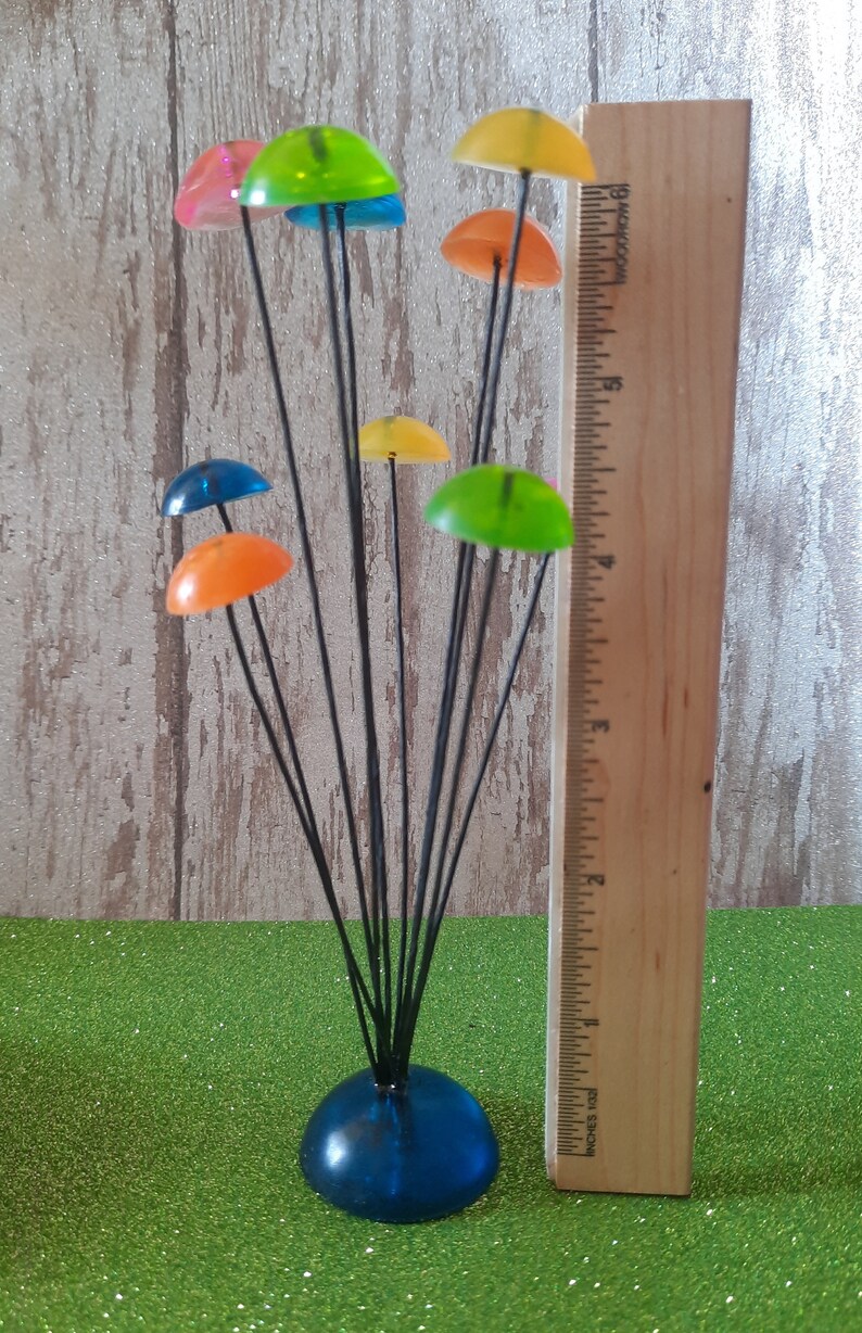 K&ouml;nnte beinhalten: Eine farbenfrohe, abstrakte Skulptur aus Glas und Metall. Die Skulptur besteht aus mehreren runden, bunten Glasteilen auf d&uuml;nnen Metallstielen. Die Stiele sind an einer blauen Glasbasis befestigt. Die Skulptur ist etwa 45 cm hoch.