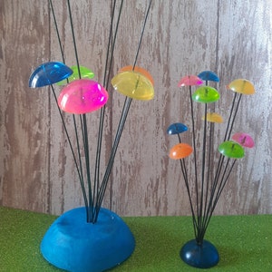 K&ouml;nnte beinhalten: Zwei farbenfrohe, skurrile Skulpturen aus durchsichtigen Plastikkuppeln auf schwarzen Metallstielen. Die gr&ouml;&szlig;ere Skulptur hat 8 Kuppeln in verschiedenen Farben, darunter Blau, Gr&uuml;n, Gelb, Orange und Pink. Die kleinere Skulptur hat 7 Kuppeln in &auml;hnlichen Farben. Beide Skulpturen haben eine blaue Basis.