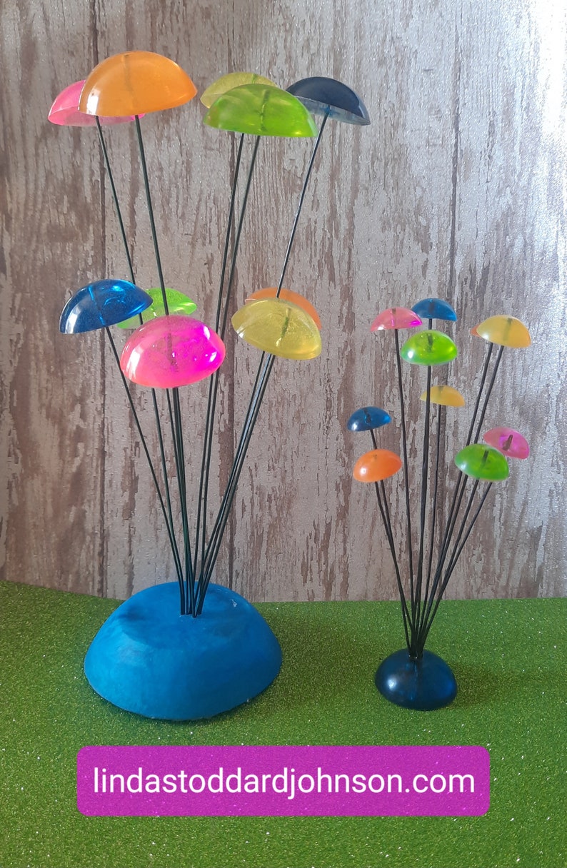 K&ouml;nnte beinhalten: Zwei farbenfrohe, skurrile Skulpturen aus durchsichtigen Plastikkuppeln auf schwarzen Metallstielen. Die gr&ouml;&szlig;ere Skulptur hat 8 Kuppeln in verschiedenen Farben, darunter Blau, Gr&uuml;n, Gelb, Orange und Pink. Die kleinere Skulptur hat 7 Kuppeln in &auml;hnlichen Farben. Beide Skulpturen haben eine blaue Basis.