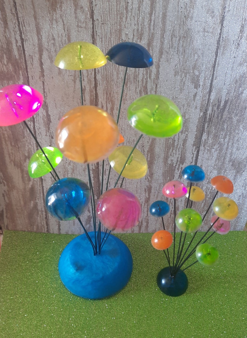 K&ouml;nnte beinhalten: Eine farbenfrohe, skurrile Skulptur aus klaren, durchsichtigen Kugeln auf Drahtstangen. Die Kugeln sind in verschiedenen Farben, darunter rosa, blau, gr&uuml;n, gelb und orange. Die Skulptur steht auf einem blauen Sockel.