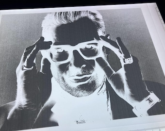 May include: Black and white portrait of a person wearing square-framed glasses, with hands touching the frames. The person has a beard and is wearing a watch and rings. The image is a high-contrast, grayscale photograph.