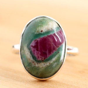 Op de afbeelding: Een zilveren ring met een ovale groene en roze edelsteen. De edelsteen heeft een uniek patroon van groen en roze.