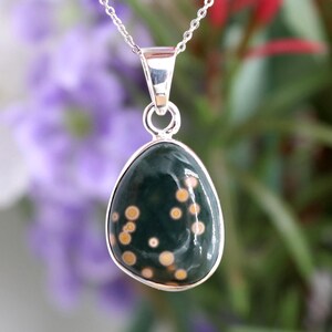 May include: A silver chain necklace with a green and gold oval pendant. The pendant has a speckled pattern of gold dots on a dark green background.