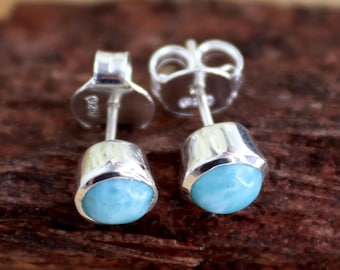 May include: A pair of silver stud earrings featuring round blue gemstones. The earrings have a simple design and are ideal for everyday wear.
