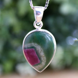 Könnte beinhalten: Eine silberne Halskette mit einem Anhänger in Tropfenform mit einem grün-rosa Edelstein. Der Edelstein hat ein weißes Spiralmuster und eine rosa Mitte.