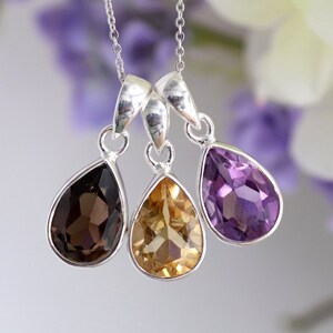 K&ouml;nnte beinhalten: Eine silberne Halskette mit drei tropfenf&ouml;rmigen Anh&auml;ngern. Die Anh&auml;nger sind aus Rauchquarz, Citrin und Amethyst.