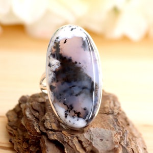 May include: A silver ring featuring a large oval dendritic agate gemstone. The agate is white, grey, and black with a swirling pattern.