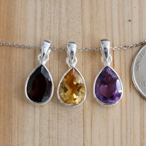 K&ouml;nnte beinhalten: Drei silberne Tropfenanh&auml;nger mit verschiedenen farbigen Edelsteinen. Die Anh&auml;nger befinden sich an einer silbernen Kette und h&auml;ngen vor einem h&ouml;lzernen Hintergrund. Die Edelsteine sind Amethyst, Citrin und Rauchquarz.