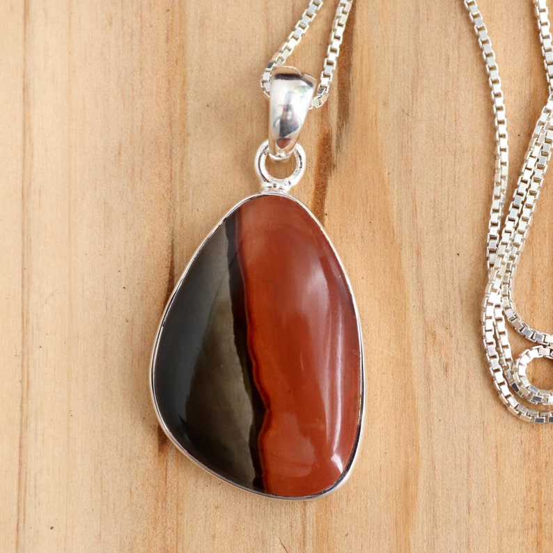 May include: A silver chain necklace with a teardrop-shaped pendant featuring a red, black, and gray banded gemstone.