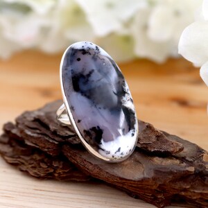 May include: A silver ring featuring a large oval dendritic agate gemstone. The agate displays a blend of white, grey, and black hues.