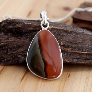 May include: A teardrop-shaped pendant with a silver bail and a red, black, and gray banded stone.