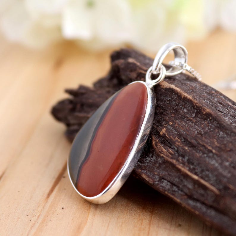May include: A silver pendant with a red and black agate stone. The stone is set in a silver bezel and has a teardrop shape.