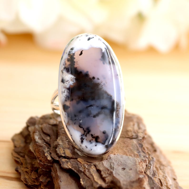 May include: A silver ring featuring a large oval dendritic agate gemstone. The agate is white, grey, and black with a swirling pattern.
