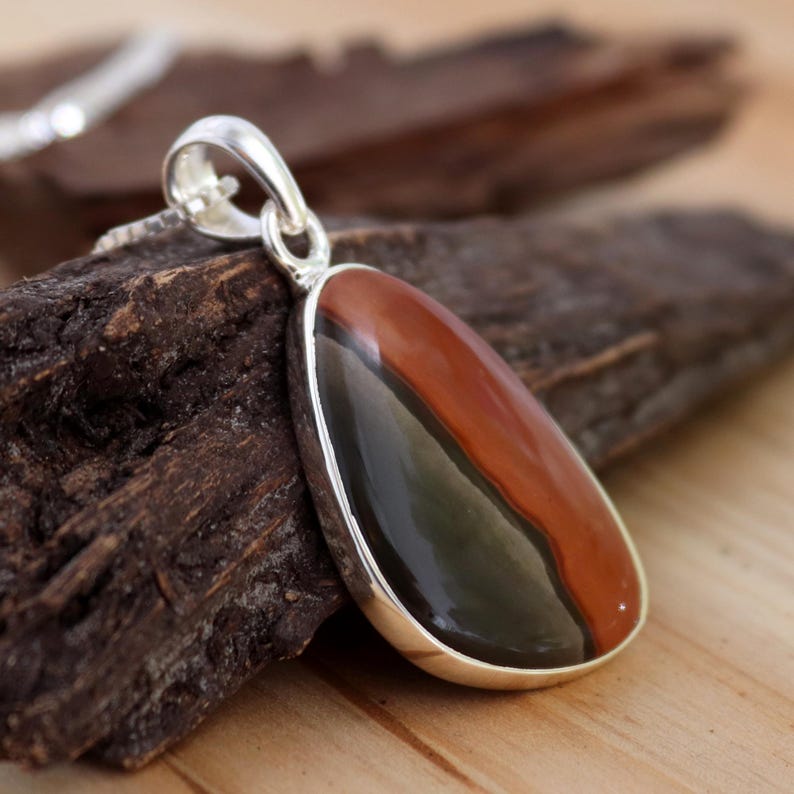 May include: A silver pendant with a teardrop-shaped stone featuring a black, green, and red banded pattern.