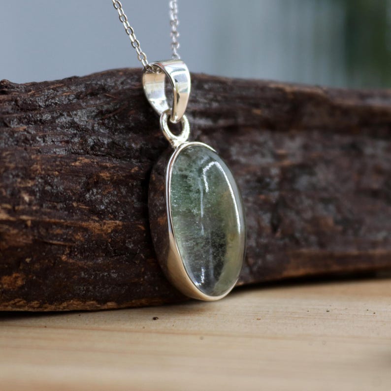 May include: A silver chain necklace with a green oval pendant. The pendant is set in a silver bezel and has a clear, faceted stone.