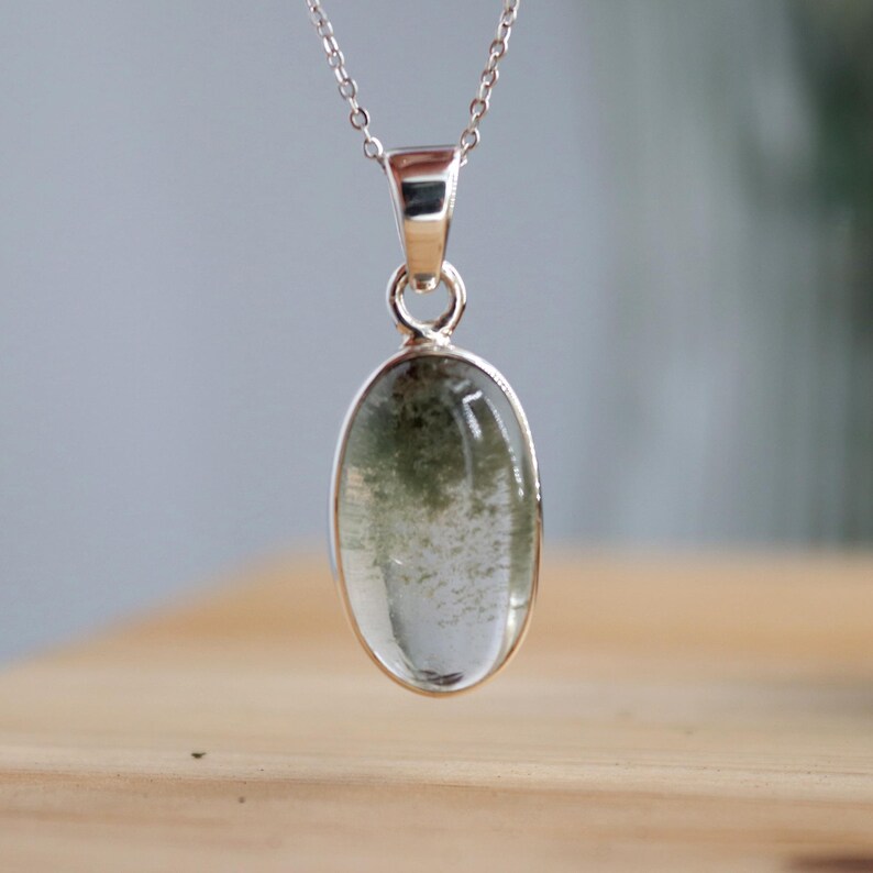 May include: A silver chain necklace with a green and clear oval pendant. The pendant is set in a silver bezel.