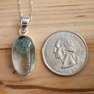 May include: A silver chain necklace with a green and clear oval pendant. The pendant is about the size of a US quarter.