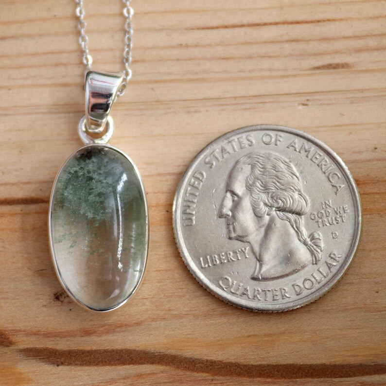 May include: A silver chain necklace with a green and clear oval pendant. The pendant is about the size of a US quarter.