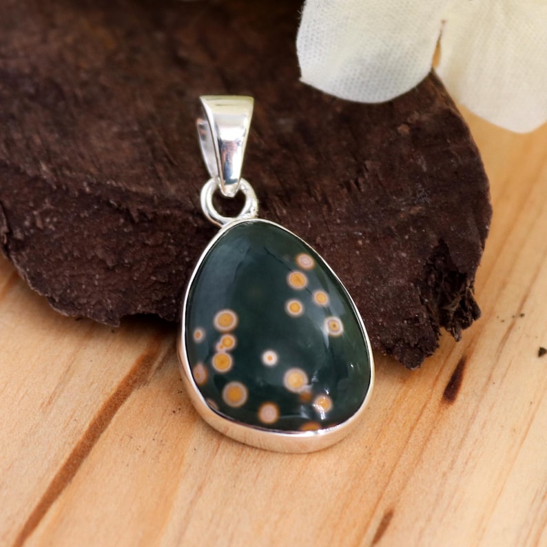 May include: A silver pendant with a green and brown stone. The stone is oval shaped and has a speckled pattern.