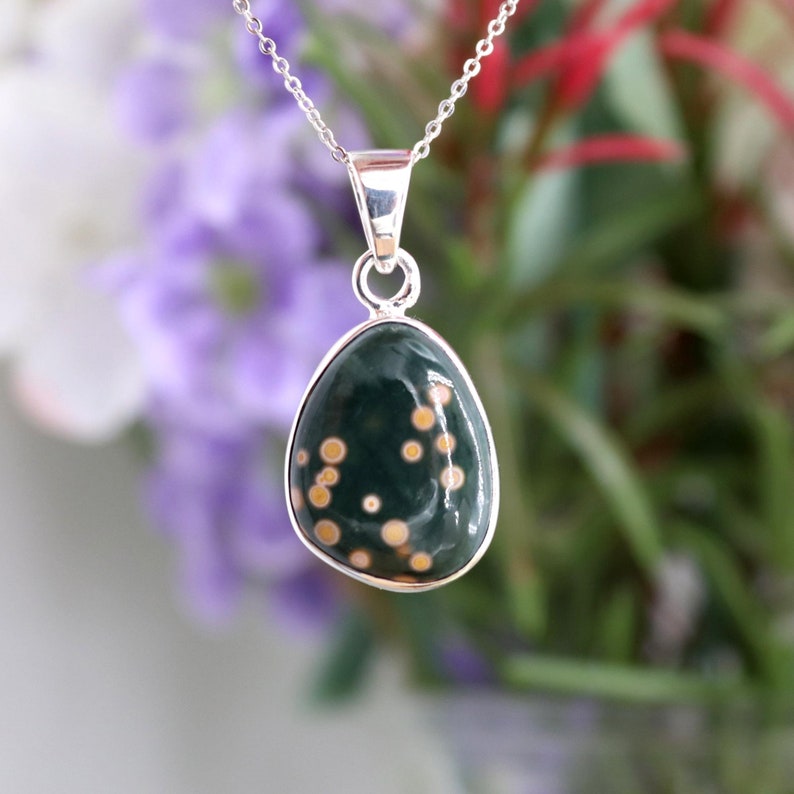 May include: A silver chain necklace with a green and gold oval pendant. The pendant has a speckled pattern of gold dots on a dark green background.
