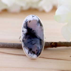 May include: A silver ring featuring a large oval-shaped black and white agate gemstone. The ring is displayed on a wooden surface.
