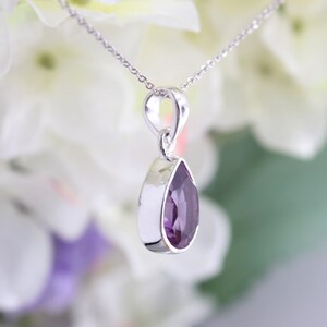 K&ouml;nnte beinhalten: Eine silberne Halskette mit einem Anh&auml;nger in Form einer Birne, besetzt mit einem Amethyst. Der Anh&auml;nger h&auml;ngt an einer silbernen Kette.