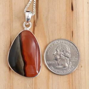 May include: A silver pendant featuring a red, black, and gray banded agate stone. The pendant is approximately the size of a US quarter.