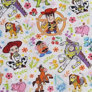 May include: A white fabric with a repeating pattern of Toy Story characters, including Woody, Buzz Lightyear, Jessie, and Rex. The characters are surrounded by colorful flowers and leaves.