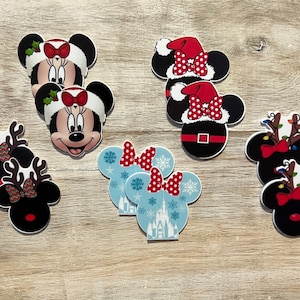 以下が含まれることがあります： クリスマスをテーマにしたミニーマウスの頭の切り抜きセット。切り抜きには、サンタ帽子のミニーマウス、トナカイのヘッドバンドをしたミニーマウス、雪片と城が描かれた冬のヘッドバンドをしたミニーマウスがいます。