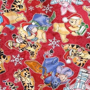 Puede incluir: Tela roja con un patrón repetido de varios personajes de Disney, incluyendo Winnie the Pooh, Tigger, Eeyore y Piglet. Los personajes llevan gorros de Papá Noel y están rodeados de copos de nieve.