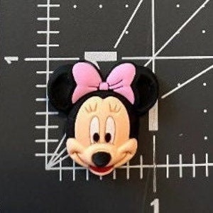 May include: A cartoon character head of Minnie Mouse with black ears, a pink bow, and a smiling face.