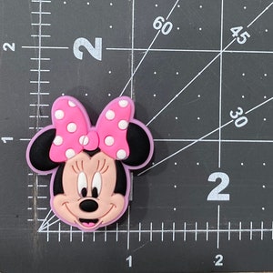 Puede incluir: Un personaje de Minnie Mouse rosa y negro con un lazo rosa con lunares blancos.