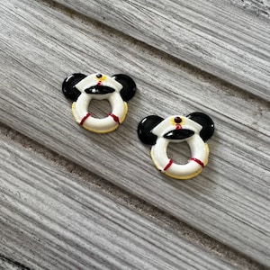 May include: Two black and white life preserver charms with red accents. The charms are shaped like a life preserver with Mickey Mouse ears.