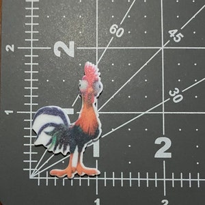 May include: A colorful rooster figurine with a white, green, and black tail, orange and red feathers, and a white face with black eyes.