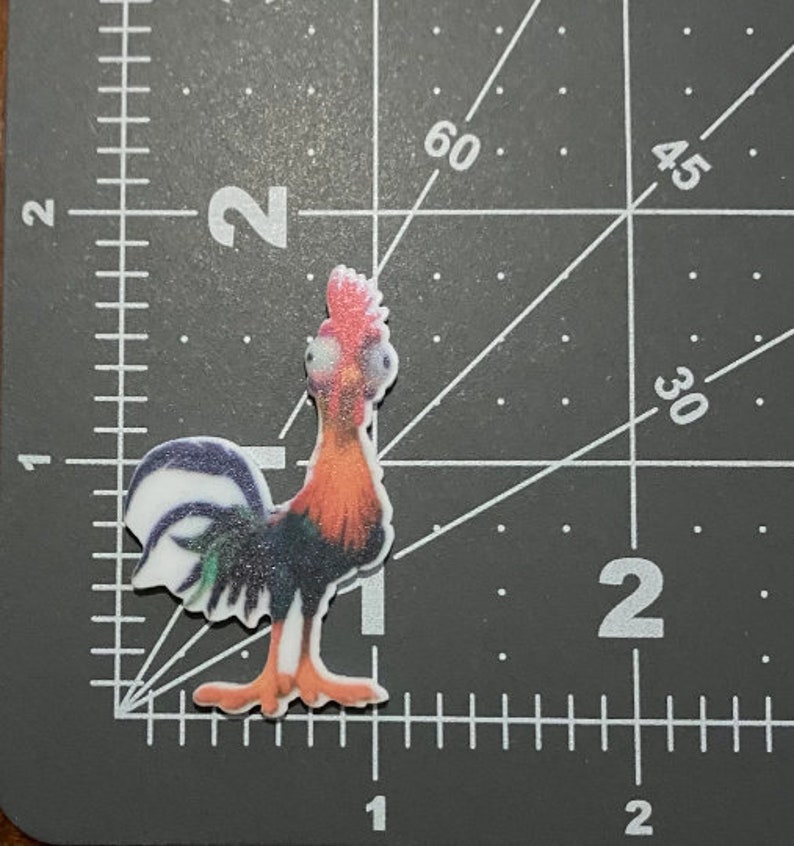 May include: A colorful rooster figurine with a white, green, and black tail, orange and red feathers, and a white face with black eyes.