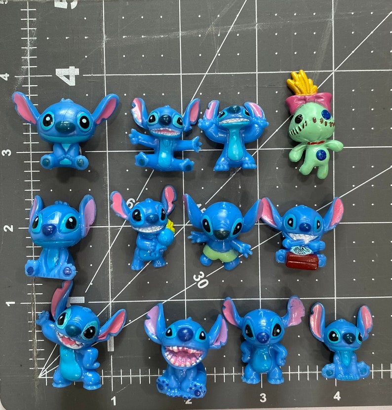 May include: A collection of 11 blue Stitch figurines, including a green Angel figurine. The Stitch figurines are in various poses, some holding objects like a flower and a book. The figurines are made of plastic and have a glossy finish.