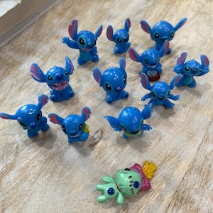 May include: A collection of 12 blue Stitch figurines, some with different poses and expressions. There is also a green Stitch figurine with a pink and yellow design.
