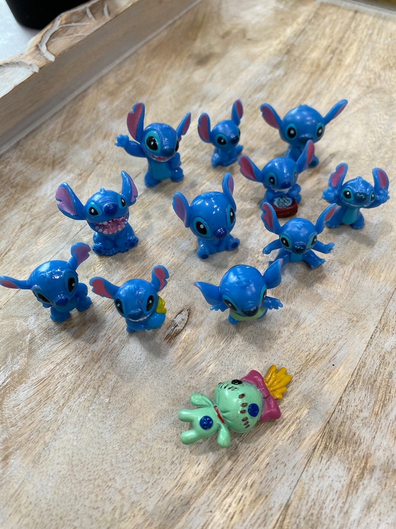 May include: A collection of 12 blue Stitch figurines, some with different poses and expressions. There is also a green Stitch figurine with a pink and yellow design.