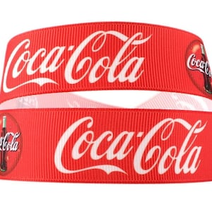 May include: Red and white ribbon with the Coca-Cola logo and a bottle of Coca-Cola printed on it.
