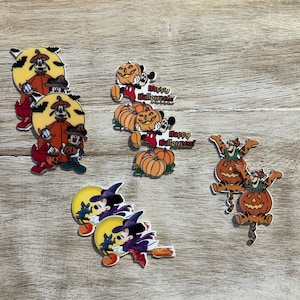 Puede incluir: Un conjunto de 10 cabujones de resina con temática de Halloween que representan a Mickey Mouse, Goofy y un tigre. Los cabujones están decorados con calabazas, murciélagos y la frase "Happy Halloween".