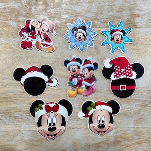 Puede incluir: Conjunto de nueve pegatinas de Mickey Mouse y Minnie Mouse con temática navideña. Las pegatinas muestran a Mickey y Minnie en varias poses, incluyendo una pareja besándose, con gorros de Papá Noel y sosteniendo copos de nieve.