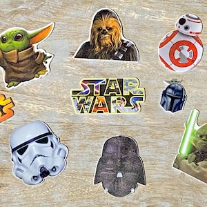 May include: A collection of Star Wars character stickers featuring Yoda, Chewbacca, BB-8, R2-D2, Darth Vader, Stormtrooper, and a Mandalorian. The stickers are on a woodgrain background.