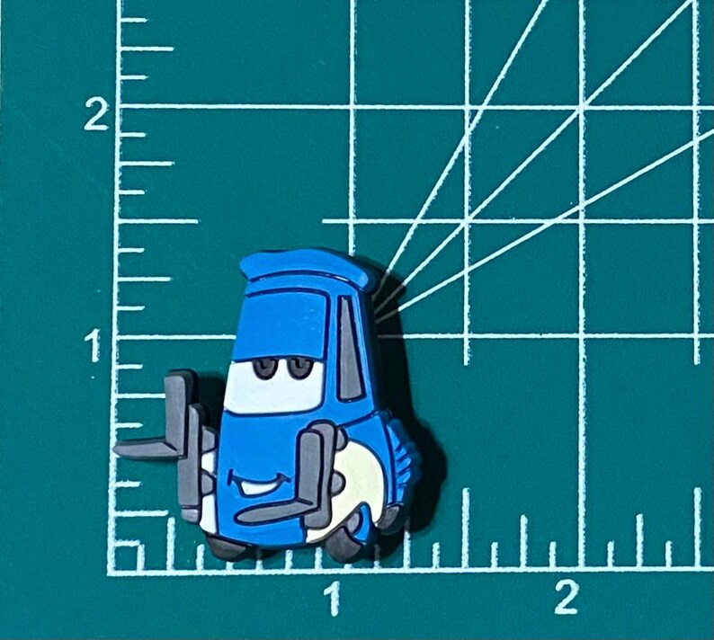 May include: A blue cartoon car with a smiling face and large eyes. The car has a white tire and a black bumper. The car is a character from the animated movie Cars.