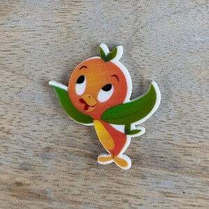 May include: A cartoon orange bird with green leaves for wings. The bird has a white face with black eyes and a yellow beak.