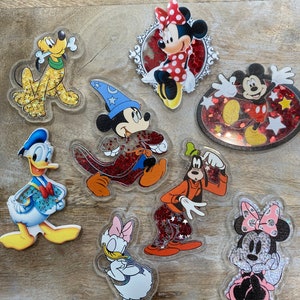 Puede incluir: Un conjunto de ocho figuritas de personajes de Disney de colores con detalles de purpurina. Los personajes incluyen Mickey Mouse, Minnie Mouse, Donald Duck, Daisy Duck, Goofy, Pluto y dos figuritas más de Minnie Mouse.