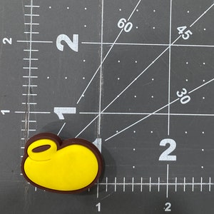 Puede incluir: Un amuleto de personaje de dibujos animados amarillo y marr&oacute;n con un lazo para sujetarlo a un llavero o bolso.