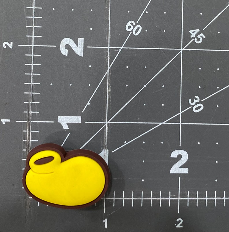 Puede incluir: Un amuleto de personaje de dibujos animados amarillo y marr&oacute;n con un lazo para sujetarlo a un llavero o bolso.