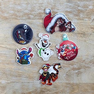 Puede incluir: Seis pegatinas con temática navideña con varios personajes de Disney. Las pegatinas incluyen un muñeco de nieve, una ardilla, un Stitch, un Jack Skellington, un Tigger y un grupo de patos en un adorno navideño.